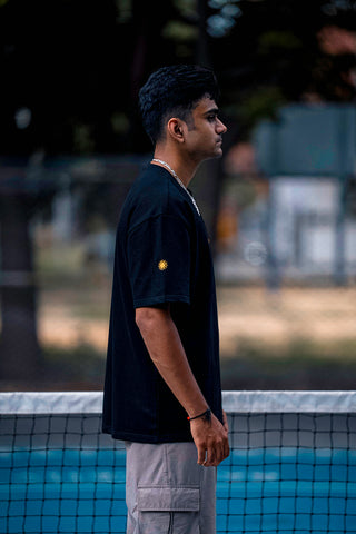 A man in a black t-shirt standing on a pickleball court.