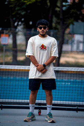 A man wearing a beige shirt with an elephant print on the front standing on a pickleball court