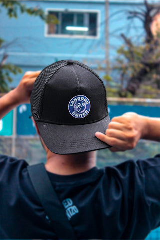 An outdoor image of a person viewed from back wearing a black trucker hat with a circular purple and white 'Langoor United' logo on the front.