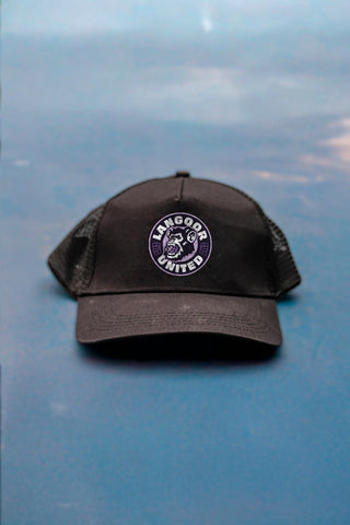 A black trucker-style cap with a circular embroidered 'Langoor United' logo on the front, on the floor of a pickleball court.