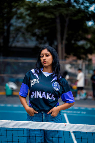Girl wearing a black and purple sports jersey with 'Pinaka' on a pickleball court