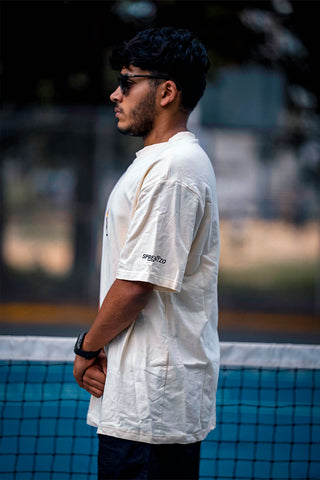 A man wearing a beige shirt with an elephant print on the front standing on a pickleball court